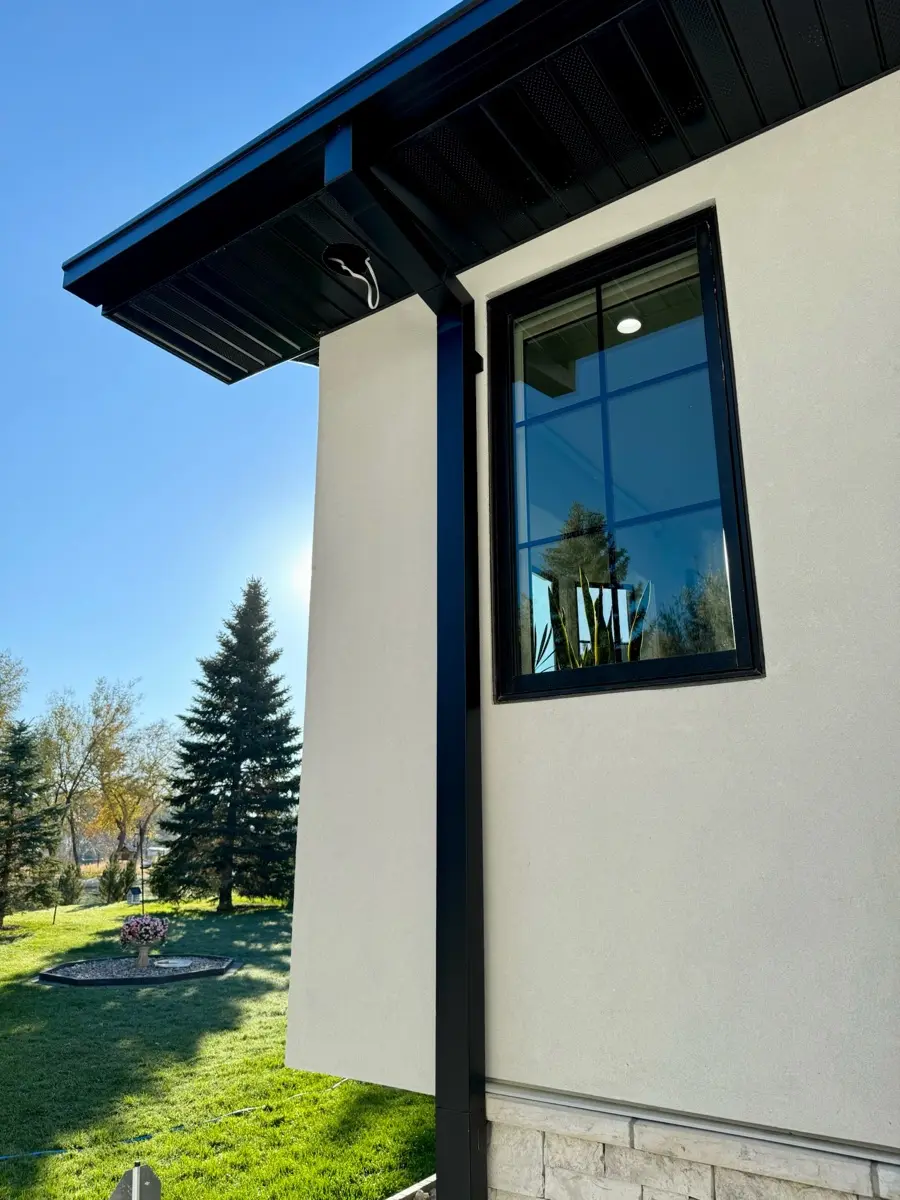 Black seamless gutters on a stucco home under mature trees